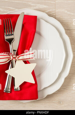 Festive Christmas table setting place setting with white china plates, red cloth napkin and silverware on rustic wood background. Vertical with empty  Stock Photo