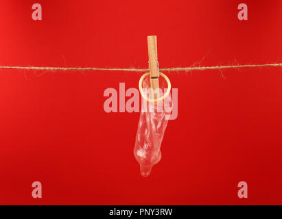 Close up one condom hanging on twine washing line with wooden clothespin over red background with copy space, low angle side view Stock Photo