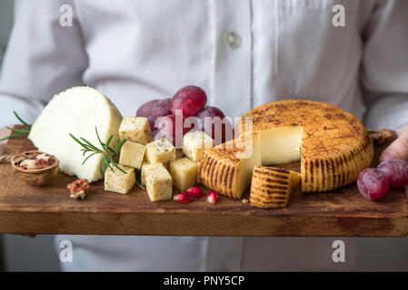 Cheese platter with assorted cheeses, grapes, nuts and hands of cheese maker on black background. Italian cheese and fruit platter. Stock Photo