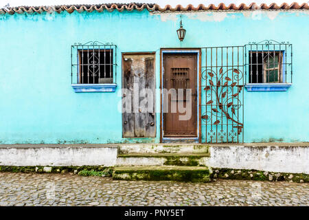 Turquoise painted house exterior with decorated wrought iron bars on windows & door in cobbled street in Guatemala, Central America Stock Photo