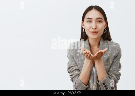 Sending sweet kisses to loving friends. Portrait of charming feminine adult woman in trendy jacket, smiling, holding palms near mouth and blowing mwah, expressing sympathy and care Stock Photo