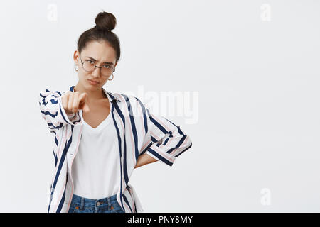 Woman blaming friend, accusing him in crime. Portrait of moody displeased attractive female model in shirt and glasses, pointing at camera, holding hand on hip and frowning from disappointment Stock Photo