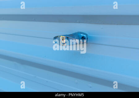 Bluish tinged image of a garage door handle at the locked position on a light colored grooved metal shutter Stock Photo
