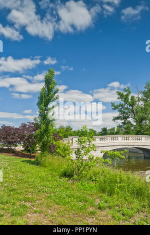 Spectacular sky over the bridge next to purple-leaf redbud trees and a poplar beside the Grand Basin at St. Louis Forest Park. Stock Photo