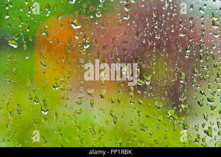 View towards an outdoor swing set through a window covered with raindrops on a summer day. Stock Photo