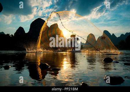 Silhouette of Cormorant fisherman using net on the ancient bamboo boat Stock Photo