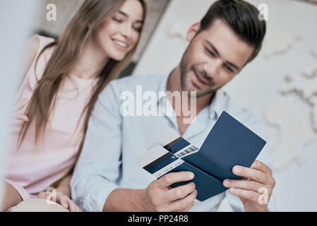 Travel agent and young couple. Young woman smiling and reviwing tickets, passport with visa. Travel agency office interior with big world map in backgrownd Stock Photo