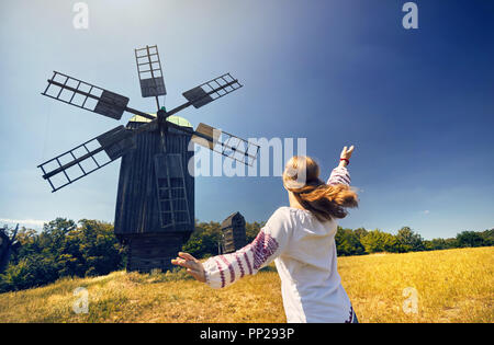 Beautiful Ukrainian girl dancing near wooden wind mill in white ethnic shirt at national architecture museum in Pirogovo. Kiev, Ukraine Stock Photo