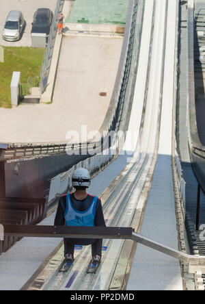 A ski jumper at Bergisel Ski Jump at Innsbruck (Austria) is getting ready for jumping off during summertime. Stock Photo