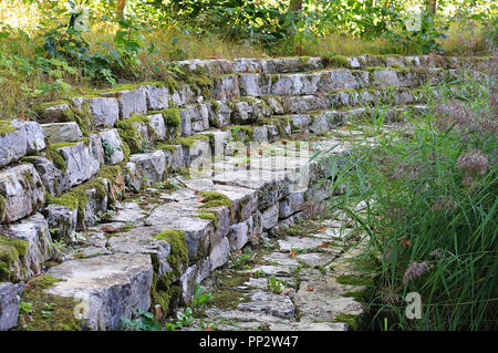 terraced limestone wall covered with moss in garden landscape with flowering reed Stock Photo