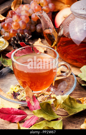 Cup with tea on an autumn background of fallen leaves, apples and grapes.Autumn postcard Stock Photo