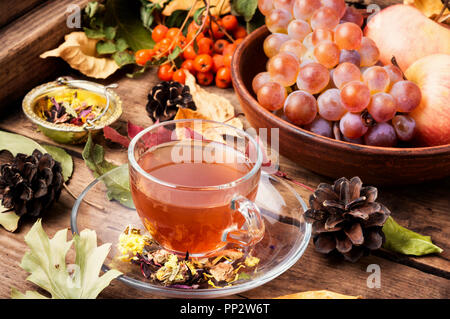 Cup with tea on an autumn background of fallen leaves, apples and grapes.Autumn still life Stock Photo