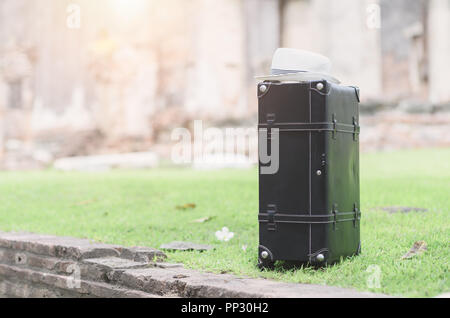 old black baggage bag with hat and on grass, old temple background and vintage tone Stock Photo