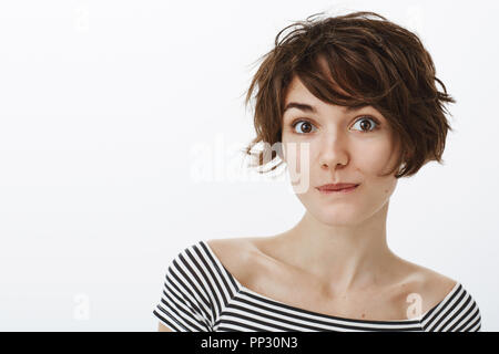 Dreamy good-looking feminine girl with short stylish haircut, smiling and smirking while gazing flirty at camera, expressing positive attitude, being amused with nice talk with guy during date Stock Photo