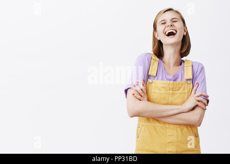 Stop joking, belly aches from laughter. Carefree relaxed and happy girlfriend with fair hair, laughing out loud, tilting head back from joy, holding hands crossed on chest, having fun with friends Stock Photo