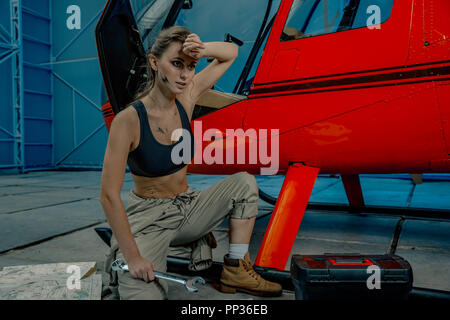 helicopter maintenance femail worker. woman pilot or helicopter mechanic holding the adjustable wrench. woman is tired after work. scattered drawings Stock Photo