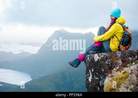 Image of tourist woman with backpack sitting on top of mountain in background of picturesque landscape during day Stock Photo