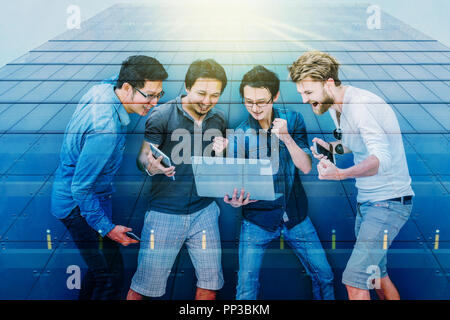 Overlab of Modern business building glass of skyscrapers and Group Of Asian and Multiethnic Business people using laptop with happy and celebrate acti Stock Photo