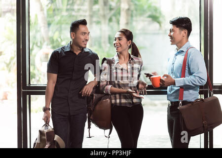 Three young and cheerful employees talking in the morning Stock Photo