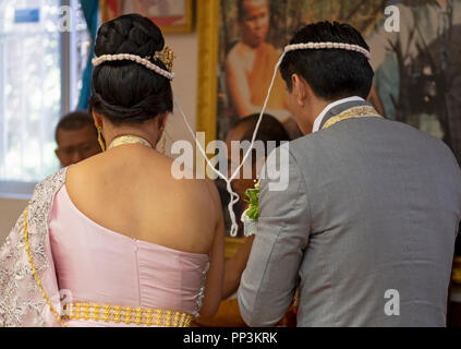 A rear view of a bride & groom during a Buddhist wedding ceremony. Their heads are tied together with sacred thread. In Elmhurst, Queens, New York. Stock Photo