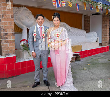 Portrait,  in front of a statue of Buddah. of Thai bride & her South American groom just after their Buddhist wedding In Elmhurst, Queens, New York. Stock Photo