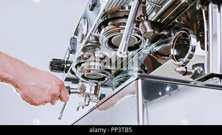 Hands of professional barista standing near the big metal coffee machine and looking how coffee pouring into the white cups Stock Photo