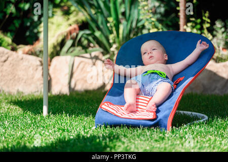 Baby boy lies on a deck-chair on green lawn. Relax and vacation concept Stock Photo