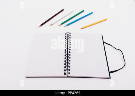 Open notepad with spring with two blank sheets on white table with colored pencils above it. Stock Photo