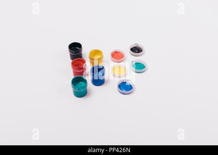 Group of multi-colored paints in open jars next to lids on solid white background, top view. Stock Photo