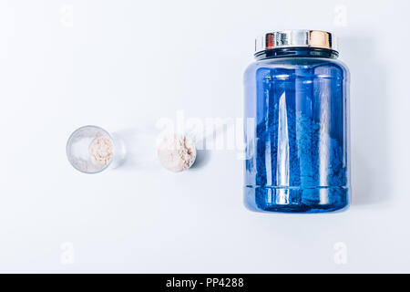 Composition of items to make protein shake, top view on white solid background. Big blue can of sport nutrition supplement powder near scoop and glass Stock Photo