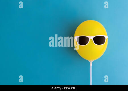 Yellow party balloon with sunglasses on a blue background Stock Photo