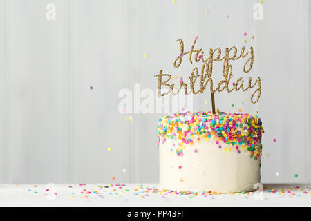 Colorful birthday cake with golden happy birthday banner and falling sprinkles Stock Photo