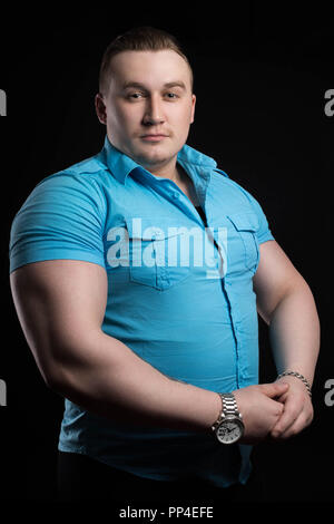 Portrait of a businessman weightlifter with large muscle in the blue shirt and cardigan on a black background. Athletic man fitness coach at power ath Stock Photo