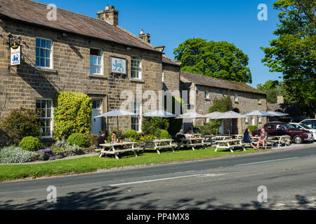 Customers enjoy alfresco drinks sitting in sun at tables under parasols outside the quaint Blue Lion Inn - East Witton, North Yorkshire, England, UK. Stock Photo