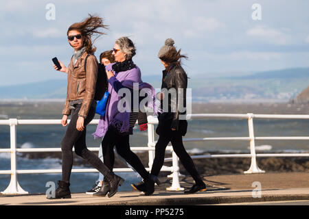 Aberystwyth, Wales, UK. Sunday 23rd Sept 2018.   UK Weather:  People walking along the promenade are windswept buffeted by the strong winds on a sunny but  blustery Equinox Sunday afternoon in Aberystwyth on the west wales coast.  Today is the last day of Astronomical Summer - when the days and night are of equal lengths. From tomorrow the nights are longer than the days, marking  the onset of Astronomical Winter in the northern hemisphere Photo © Keith Morris / Alamy Live News Stock Photo