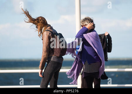 Aberystwyth, Wales, UK. Sunday 23rd Sept 2018.   UK Weather:  People walking along the promenade are windswept buffeted by the strong winds on a sunny but  blustery Equinox Sunday afternoon in Aberystwyth on the west wales coast.  Today is the last day of Astronomical Summer - when the days and night are of equal lengths. From tomorrow the nights are longer than the days, marking  the onset of Astronomical Winter in the northern hemisphere Photo © Keith Morris / Alamy Live News Stock Photo