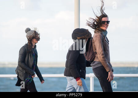 Aberystwyth, Wales, UK. Sunday 23rd Sept 2018.   UK Weather:  People walking along the promenade are windswept buffeted by the strong winds on a sunny but  blustery Equinox Sunday afternoon in Aberystwyth on the west wales coast.  Today is the last day of Astronomical Summer - when the days and night are of equal lengths. From tomorrow the nights are longer than the days, marking  the onset of Astronomical Winter in the northern hemisphere Photo © Keith Morris / Alamy Live News Stock Photo