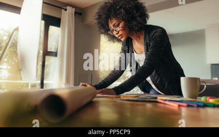 Young female architect working on a project from home office. African woman standing at the table and looking at some documents. Stock Photo