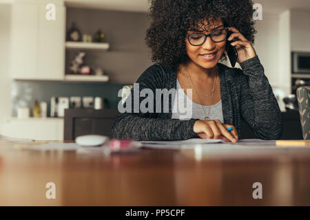 Portrait of happy young female interior designer looking at drawing and talking over smart phone. Young architect using phone at his workplace. Stock Photo
