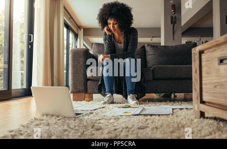 Female sitting in living room couch with few documents on floor with a laptop computer. Woman working on new business plan from home. Woman studying b Stock Photo