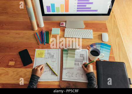 Top view of woman architect working over new blueprints at her desk. Woman with building plan, color swatches, color pencils and computer on table. Stock Photo