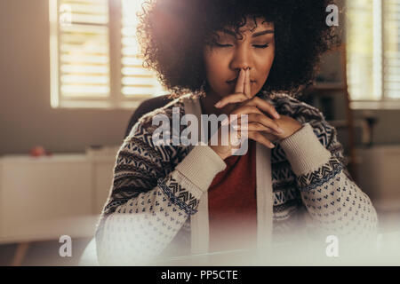 African female sitting at her work desk and thinking with her eyes closed. Stressed woman taking a break to come up with solution using mindfulness. Stock Photo