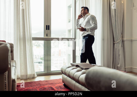 Businessman staying in hotel room and talking on mobile phone. CEO speaking on his cellphone in hotel room during business travel. Stock Photo