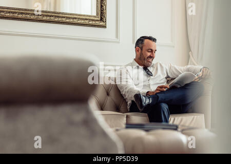 Handsome mature businessman reading a magazine while relaxing in hotel room. Man on business trip staying in a hotel. Stock Photo