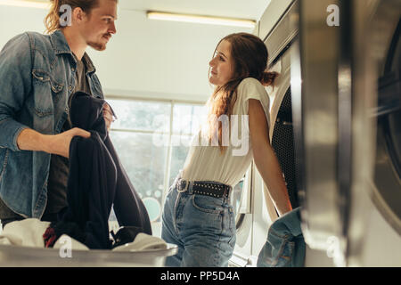 Couple standing in a laundry room looking at each other. Happy couple doing laundry together. Stock Photo
