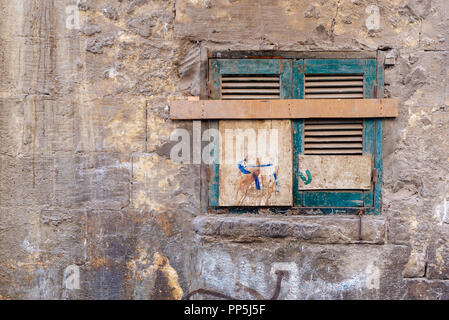 Old grunge window with closed green broken shutters on dirty cracked bricks stone wall Stock Photo