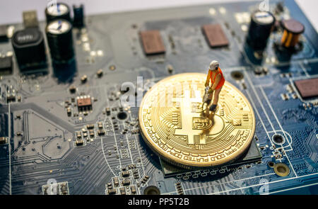 Miniature construction worker standing on physical Bitcoin, mining concept Stock Photo