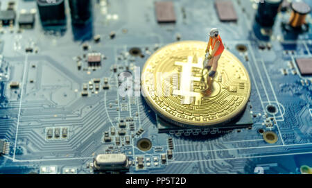 Miniature construction worker standing on physical Bitcoin, mining concept Stock Photo