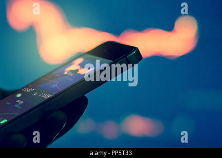 Trader in dark using mobile phone against stock market charts Stock Photo