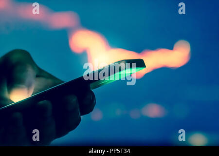 Trader in dark using mobile phone against stock market charts Stock Photo